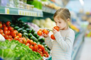 Mädchen nutzt beim Einkauf im Supermarkt ihre Sinne und riecht an einer Tomate
