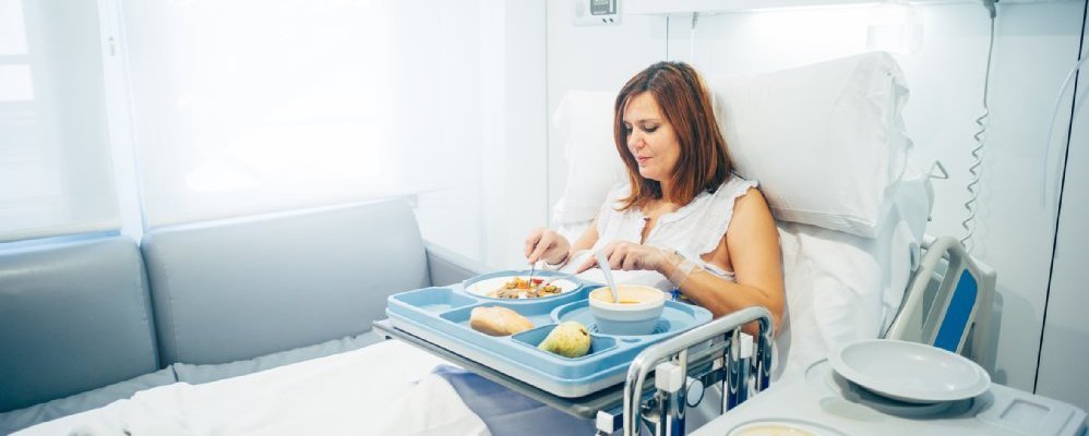Frau sitzt in einem Krankenhausbett und isst.
