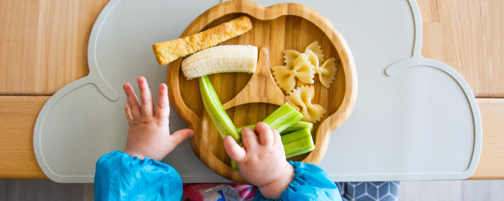 Babyhände greifen auf Teller mit mundgerechten Stücken verschiedener Lebensmittel