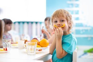 Ein fröhlicher Junge sitzt am Tisch und isst ein Stück gelbe Parika