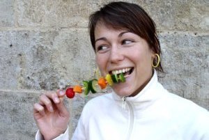 Frau isst lachend Gemüsespieß