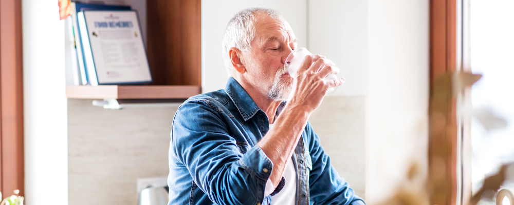 älterer Mann trinkt ein Glas Wasser in der Küche