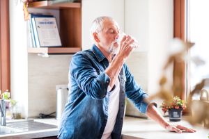 älterer Mann trinkt ein Glas Wasser in der Küche
