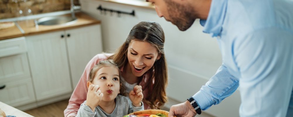 Kind isst mit Mutter und Vater Rohkost in der Küche