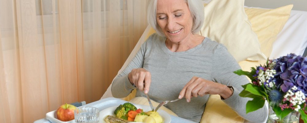 Seniorin isst im Krankenhausbett