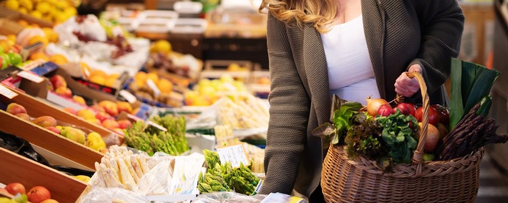 Frau kauft frisches Gemüse in Bio-Markt mit Einkaufskorb