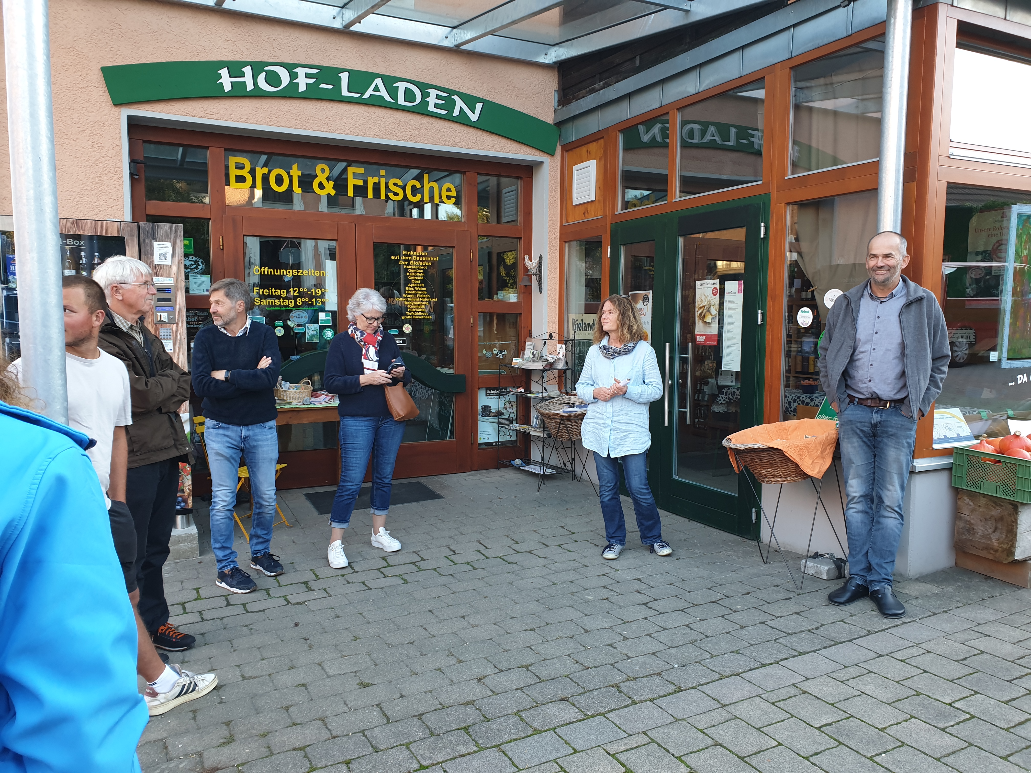 Die Besucher sowie Judith und Thomas Gebhardt stehen vor dem Laden unter der neuen Überdachung. Über der Tür steht ein Schild mit 