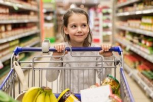 Mädchen schiebt einen Einkaufswagen mit Lebensmitteln durch einen Supermarkt