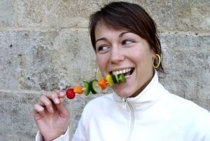 Frau isst lachend Gemüseschaschlikspieß