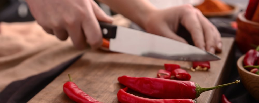 rote Chili-Schote wir mit großem Messer auf Holzbrett geschnitten
