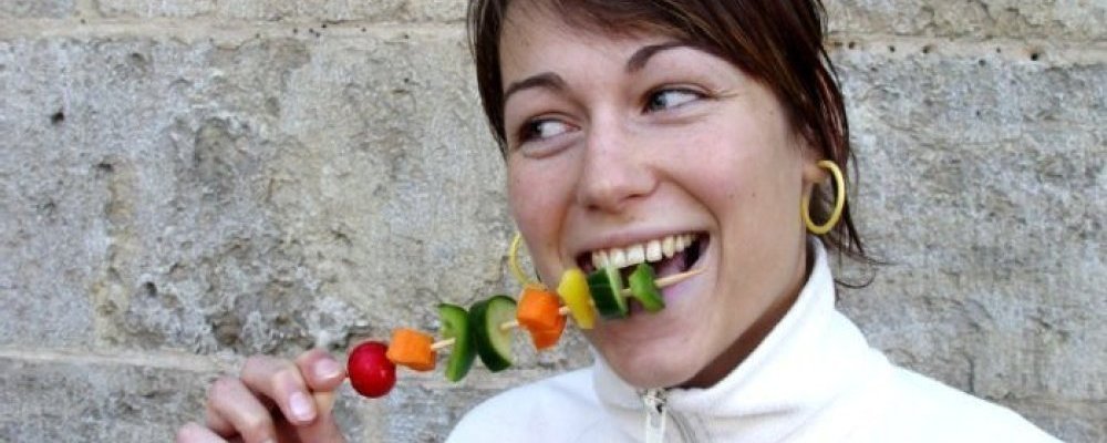 Frau isst lachend Gemüseschaschlikspieß