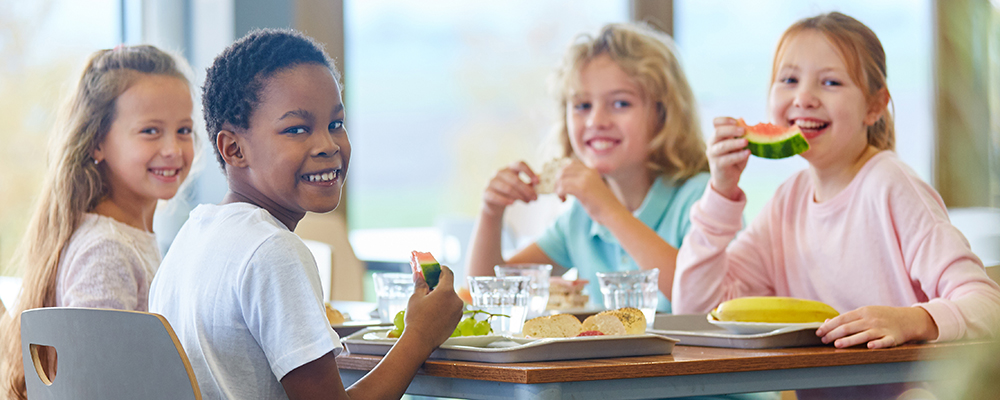 4 Schulkinder essen fröhlich in der Schulmensa