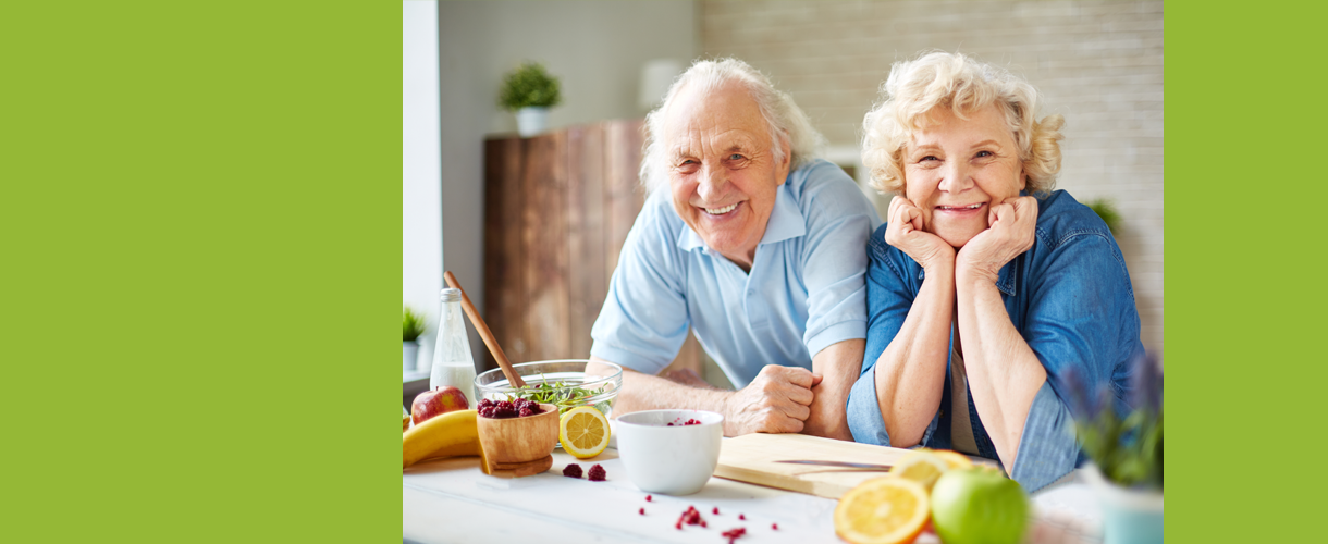 Eine Seniorin und ein Senior lehnen sich lächelnd auf den Küchentresen