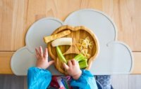 Babyhände greifen auf Teller mit mundgerechten Stücken verschiedener Lebensmittel